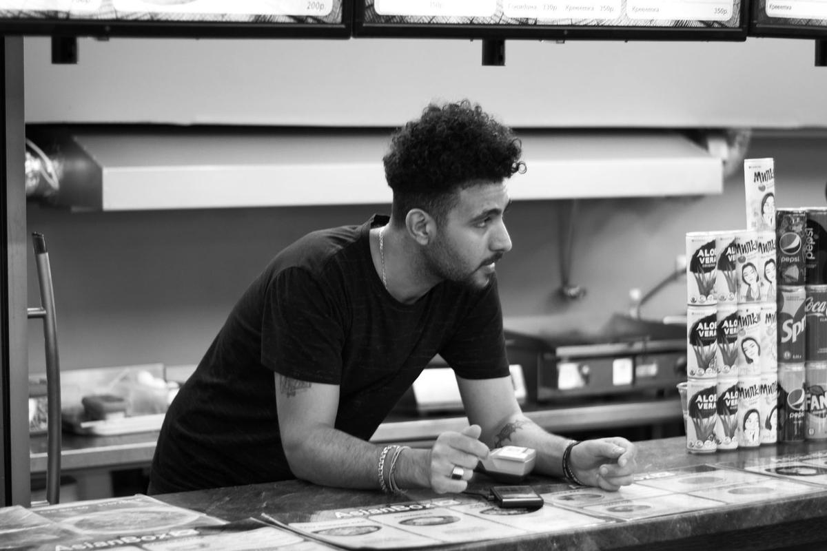 Homme en noir dans un restaurant, regardant un menu, poêle et boîtes de soda en arrière-plan Homme en noir dans un restaurant, regardant un menu, poêle et boîtes de soda en arrière-plan
