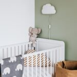 Berceau avec peluche et coussins, lampe nuage sur mur vert, panier en osier