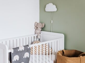 Berceau avec peluche et coussins, lampe nuage sur mur vert, panier en osier