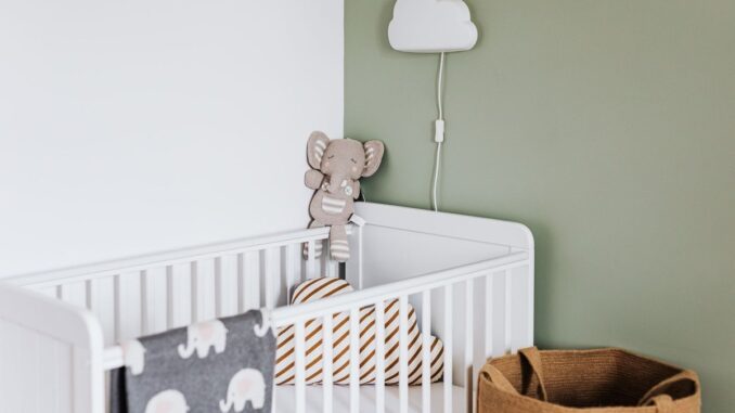 Berceau avec peluche et coussins, lampe nuage sur mur vert, panier en osier