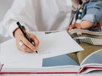 Une main écrit sur du papier, un livre ouvert, une personne tient un enfant