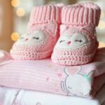 Chaussons tricotés roses avec visages d'hiboux sur vêtements bébé pliés