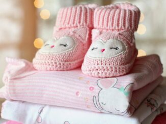 Chaussons tricotés roses avec visages d'hiboux sur vêtements bébé pliés