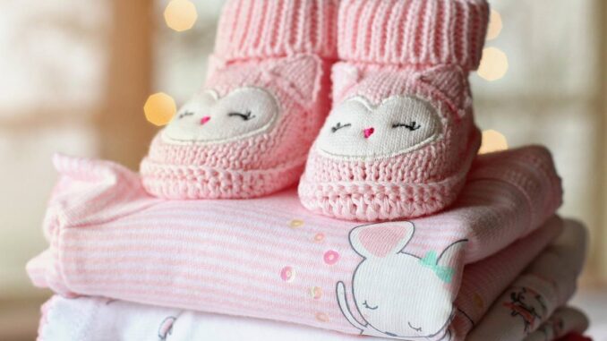 Chaussons tricotés roses avec visages d'hiboux sur vêtements bébé pliés