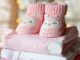 Chaussons tricotés roses avec visages d'hiboux sur vêtements bébé pliés